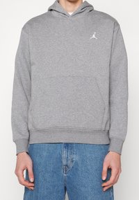 Gray hoodie made from soft fabric with a kangaroo pocket, featuring a white Jumpman logo on the chest and ribbed cuffs and hem.