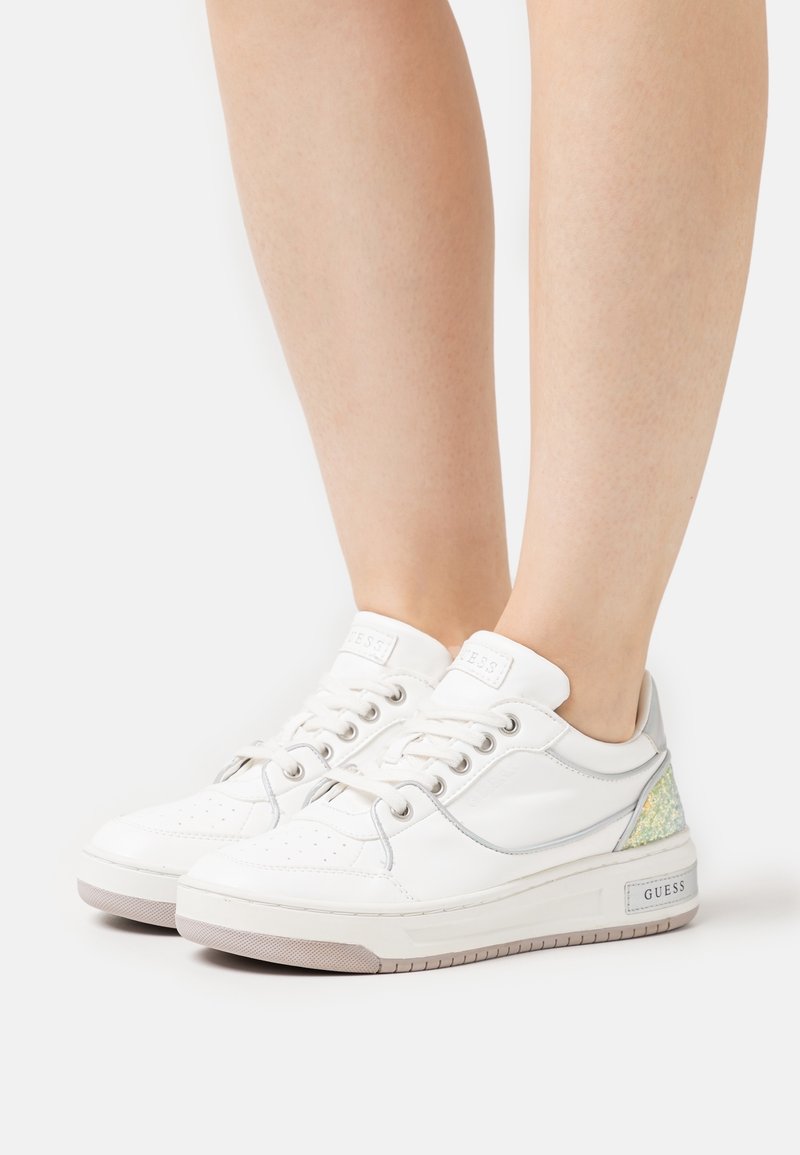 Weiße synthetische Sneakers mit silbernen Akzenten, die über perforierte Details, eine Schnürverschluss und ein strukturiertes, schillerndes Patch an der Ferse verfügen.