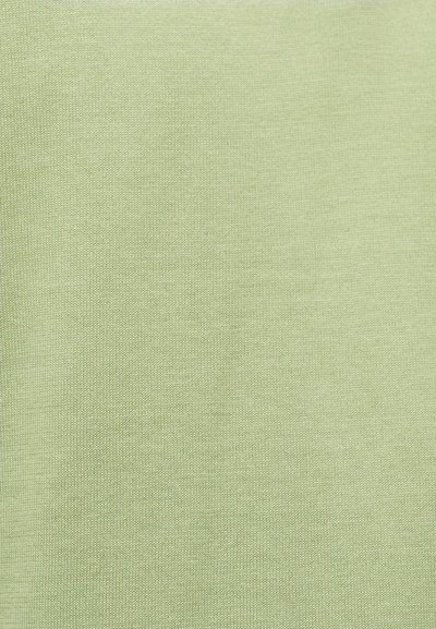 Gros plan sur un tissu vert clair à texture fine tricotée, montrant une couture uniforme et un matériau doux.