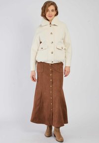 Biała wełniana kurtka z kołnierzem ze sztucznego futra i dużymi przednimi kieszeniami; brązowa zamszowa długa spódnica z guzikami z przodu i kieszeniami po bokach; beżowe botki za kostkę.