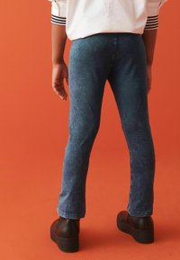 Tmavomodré denimové súpravy s slim fit strihom, s vydratým vzhľadom. V kombinácii s čiernymi platformovými topánkami na oranžovom pozadí.