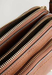 Sac à main marron à plusieurs compartiments avec des zips dorés métalliques et un matériau texturé semblable au cuir, comportant trois sections distinctes avec fermeture éclair.