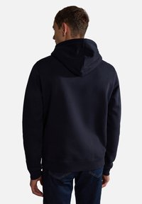 Sudadera azul marino con un corte relajado, textura suave, puños y dobladillo acanalados, y una gran capucha, llevada sobre unos jeans oscuros.