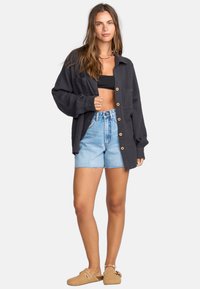 Zwarte overhemd met knopen en twee borstzakken, gemaakt van lichtgewicht materiaal, ontspannen pasvorm, gecombineerd met high-waisted denim shorts en lichtbruine instappers.