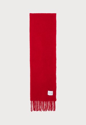 Červený šál vyrobený z měkké, strukturované tkaniny. Má dlouhé třásně na obou koncích a malou bílou značkovou etiketu přišitou na jedné straně.
