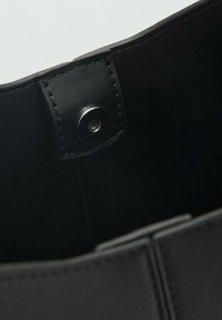 Dettaglio ravvicinato dell'interno di una borsa in pelle nera, con un robusto bottone a calamita e bordi cuciti, che mette in mostra una texture liscia.