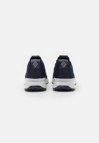Marinblå träningsskor med strukturerad stickad ovandel, mockadetaljer, vit mellansula och logotypdetalj på hälen. Mjuk textur, modern design.
