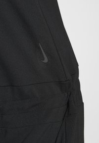 Pantalons de sport noirs en tissu lisse. Présente un discret logo swoosh noir de Nike et des coutures ajustées pour un look cintré.