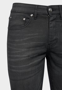 Jean en denim noir avec un design ajusté, cinq poches et des accessoires en métal argenté, dotés d'une texture subtile et de détails de décoloration.