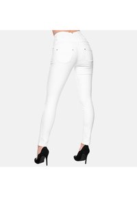 Jean skinny blanc avec une taille haute et des poches arrière, en tissu extensible, associée à des chaussures à talons hauts noires.