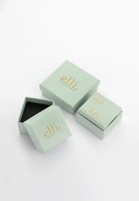 Grüne Papierverschenkboxen mit goldener Schrift, eine leicht geöffnet, die ein schwarzes Innenleben zeigt. Rechteckige und hexagonale Formen, minimalistisches Design.