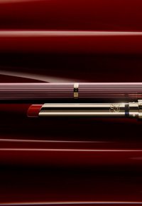 Un rouge à lèvres avec un tube en or élégant et une couleur rouge vif, placé à côté d'un étui violet strié avec un accent doré sur un fond rouge profond.