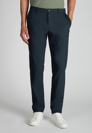 Marineblauwe broek van zacht materiaal met een slim fit, voorzien van riemlussen en een knoopsluiting. Gecombineerd met witte sneakers.