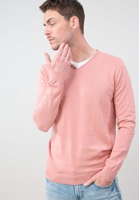 Pull léger rose en V, fabriqué dans un matériau doux, avec des manches longues et un ourlet côtelé. Inclut deux boutons près de l'encolure.