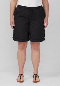 Schwarze knielange Shorts mit einem elastischen Bund, Kordelzug und umgeschlagenen Säumen, aus leichtem Stoff. Getragen mit schwarzen Zehentrenner-Sandalen.