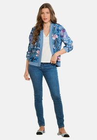 Zils ziedu raksta bomber stila jaka ar garām piedurknēm, ribveida aprocēm un jostasvietu; valkāta virs baltas virsdrēbes, kopā ar zilām džinsu biksēm un divtoņu dzīvokļiem.