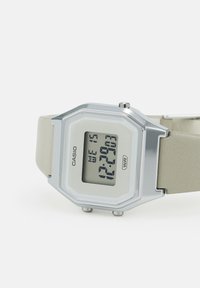 Montre numérique Casio avec un boîtier octogonal en argent, un bracelet en silicone gris clair, un affichage blanc et un indicateur de résistance à l'eau.