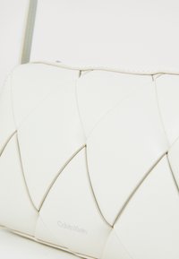 Borsa a tracolla in pelle bianca con un design trapuntato e sezioni sovrapposte. Dettaglio del logo impresso in modo discreto e una tracolla sottile.