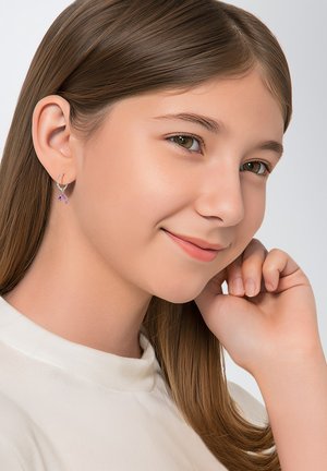 Zilveren hoepel oorbellen met een kleine paarse edelsteenaccent. Model heeft lang haar en draagt een lichtgekleurde top tegen een neutrale achtergrond.