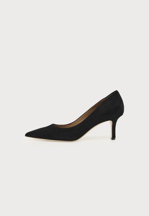 Schwarzer Wildleder-Pumps mit spitzer Zehenpartie, mittelhohem Stilettoabsatz und hellbrauner Innensohle auf hellem Hintergrund.