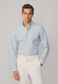 Light blue and white checkered shirt with a button-down collar, long sleeves, and a fitted design, paired with cream-colored trousers.
