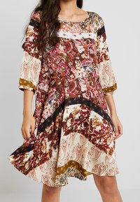 Sukienka wykonana z materiału, z rękawami o długości trzech czwartych, zdobiona kwiatowymi i paisleyowymi wzorami w kolorze czerwonym, kremowym i czarnym, z rozkloszowanym dołem i koronkowymi akcentami.