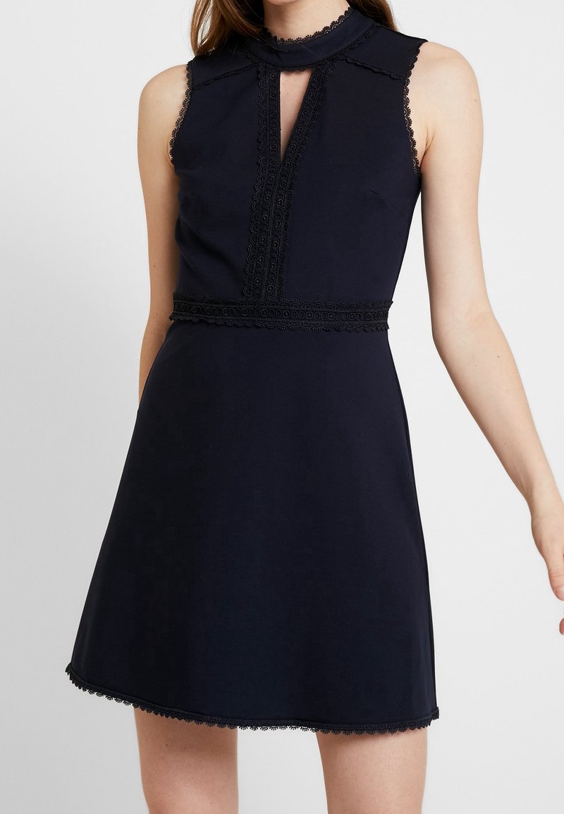 Námořnické šaty bez rukávů s vysokým výstřihem, krajkovými detaily a přiléhavým pasem, s rozšířenou sukní a detailním lemováním ve tvaru vln.