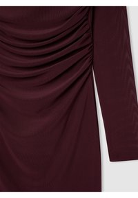 Abito borgogna, texturizzato, con maniche lunghe. Presenta dettagli arricciati sui lati, creando un effetto drappeggiato. Finitura in tessuto liscia.