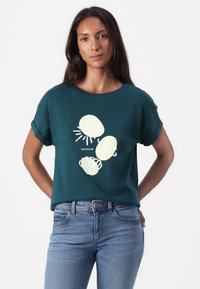 Mereroheline puuvillane t-särk, mille lühikesed käised on ülesrullitud, kaunistatud valge ja kollase kestaga ning päikesemotiividega. Sobitatud siniste teksadega.