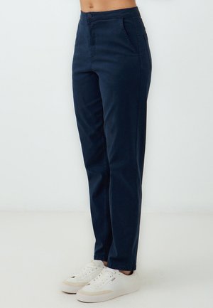 Navy blue trousers with a slim fit, front pockets, smooth texture, and a button closure, paired with white sneakers.