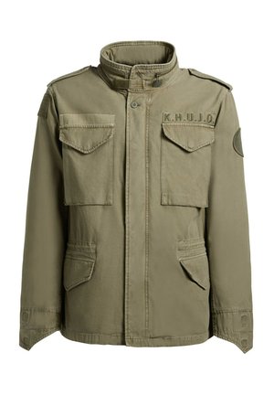 Olívazöld katonai stílusú dzseki magas gallérral, négy elülső zsebfedővel, vállpántokkal és "K.H.U.J.O" felvarróval a mellkason.