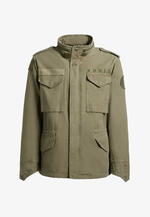 Olívazöld katonai stílusú dzseki magas gallérral, négy elülső zsebfedővel, vállpántokkal és "K.H.U.J.O" felvarróval a mellkason.