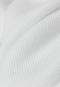 Tela blanca texturizada con un patrón de cuadrícula, que muestra una superficie lisa y ligeramente reflectante, ideal para ropa deportiva o uniformes.