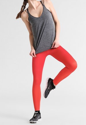 Grijs atletisch hemdje met dunne bandjes, gecombineerd met felrode legging met gestructureerde patronen. Zwarte hardloopschoenen met roze accenten.