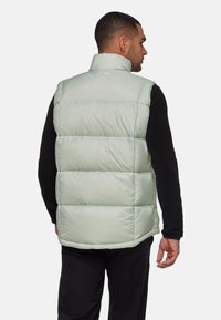 Vadderad väst i ljus mintgrön, med hög krage och horisontell sömnad. Tillverkad av slät, blankt material med en avslappnad passform.