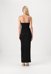 Črna brezramna maxi obleka s prilegajočim zgornjim delom, gladko teksturo in ravno silhueto, v kombinaciji s bež visokimi petami.