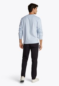 Felpa azzurro chiaro con maniche lunghe e polsini a costine, abbinata a pantaloni neri e sneaker bianche, vista da dietro.