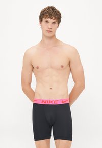 Schwarze Sportshorts mit einem dicken pinken Nike-Logo-Bund. Das Material scheint dehnbar und figurbetont zu sein, entworfen für aktive Freizeit. 