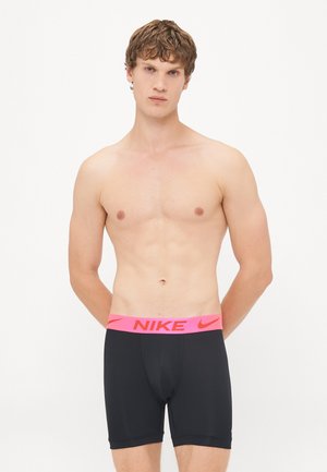 Schwarze Sportshorts mit einem dicken pinken Nike-Logo-Bund. Das Material scheint dehnbar und figurbetont zu sein, entworfen für aktive Freizeit. 