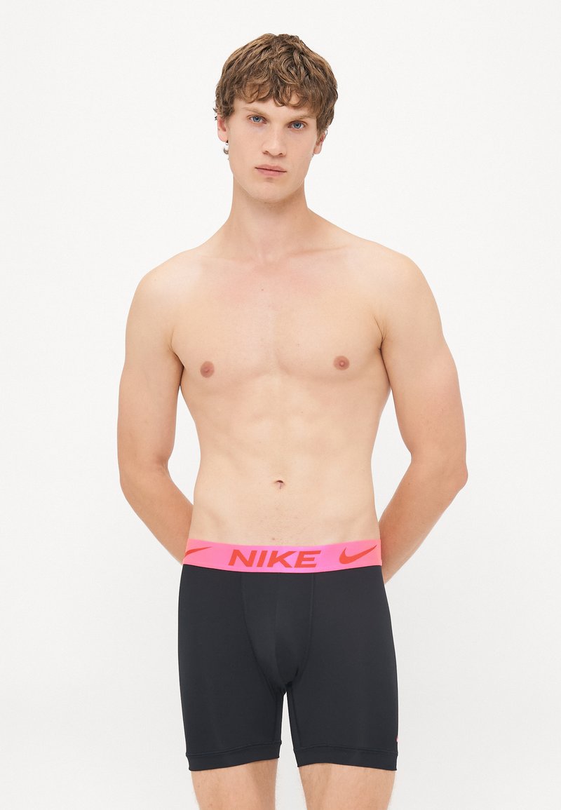 Schwarze Sportshorts mit einem dicken pinken Nike-Logo-Bund. Das Material scheint dehnbar und figurbetont zu sein, entworfen für aktive Freizeit. 