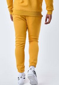 Pantalones deportivos amarillos con puños elásticos, hechos de tela suave, combinados con zapatillas blancas que tienen un logo swoosh negro.