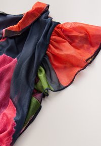 Bunt gemustertes, transparentes Stoff mit Blumenmuster, verziert mit roten und grünen Rüschen; hauptsächlich dunkelblauer Hintergrund, leicht und strukturiert.