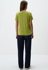 Limonkowa bluzka z krótkim rękawem i okrągłym dekoltem, o gładkiej fakturze, zestawiona z ciemnoniebieskimi spodniami o szerokich nogawkach, prezentująca swobodny styl.