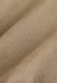 Tissu de couleur beige avec une texture fine, présentant des plis diagonaux et un léger éclat, mettant en valeur sa surface lisse et son motif tissé.