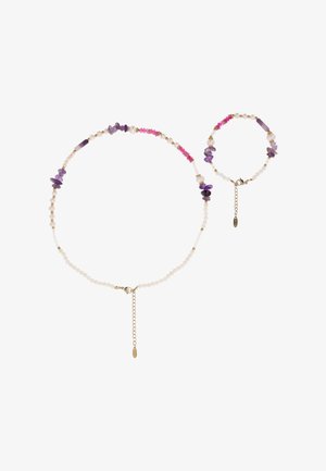 Set van halsketting en armband met witte, roze en paarse kralen met gouden kettinggespen en onregelmatige paarse steenaccenten op een witte achtergrond.