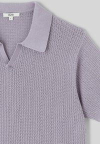 Polo à manches courtes lavande clair, avec un motif en tricot texturé, un col côtelé et un design en V. Étiquette de la marque visible sur le col.