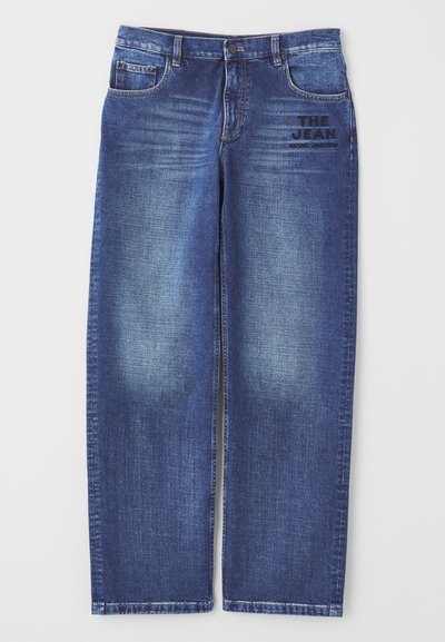 Mørkeblå denimjeans med en let slidt finish, der har fem lommer og et broderet mærke med teksten "THE JEAN" på forsiden.