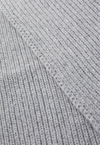 Pelēka adīta auduma, kas iezīmē vertikālas rievu līnijas. Tekstūra izskatās maiga, ar nedaudz spīdumu un vienmērīgi izvietotām šuvēm.