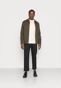 Oliven grønn knapper-skjorte over en lys genser, kombinert med sorte rette bukser og svarte sko, minimalistisch design, glatt tekstur.