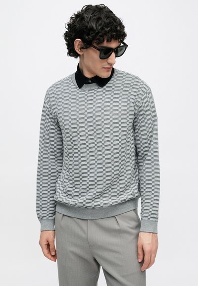 Camisola cinza com padrão e trama texturizada, gola redonda e punhos canelados. Combinada com calças cinza claro e óculos de sol pretos.